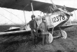 Zwei Männer mit Schutzhelm und Schutzbrillen neben einem deutschen Flugzeug mit defektem Propellor und mit der Aufschrift 